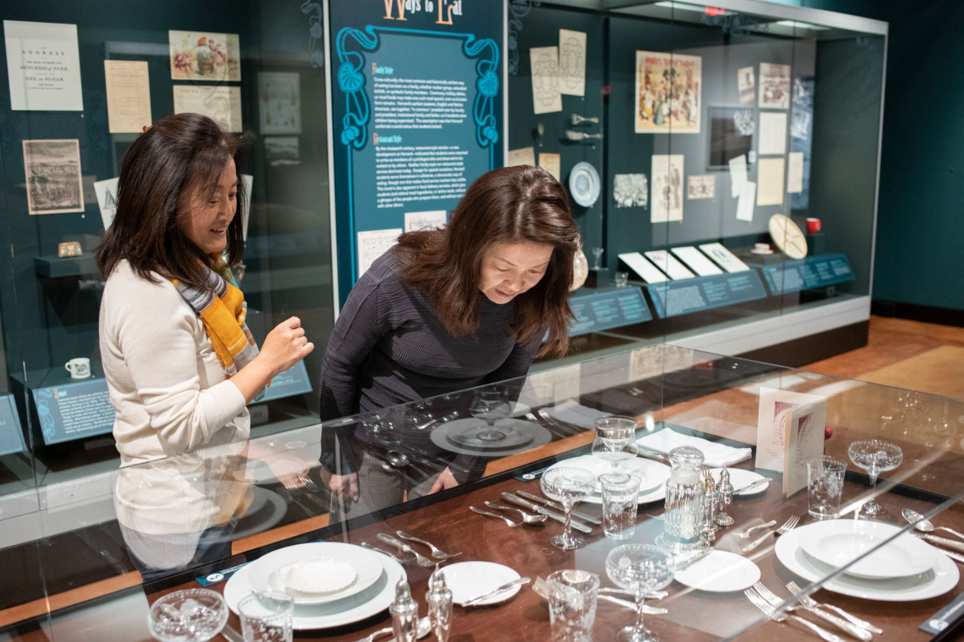 Two women peering at tableware in the Resetting The Table exhibit