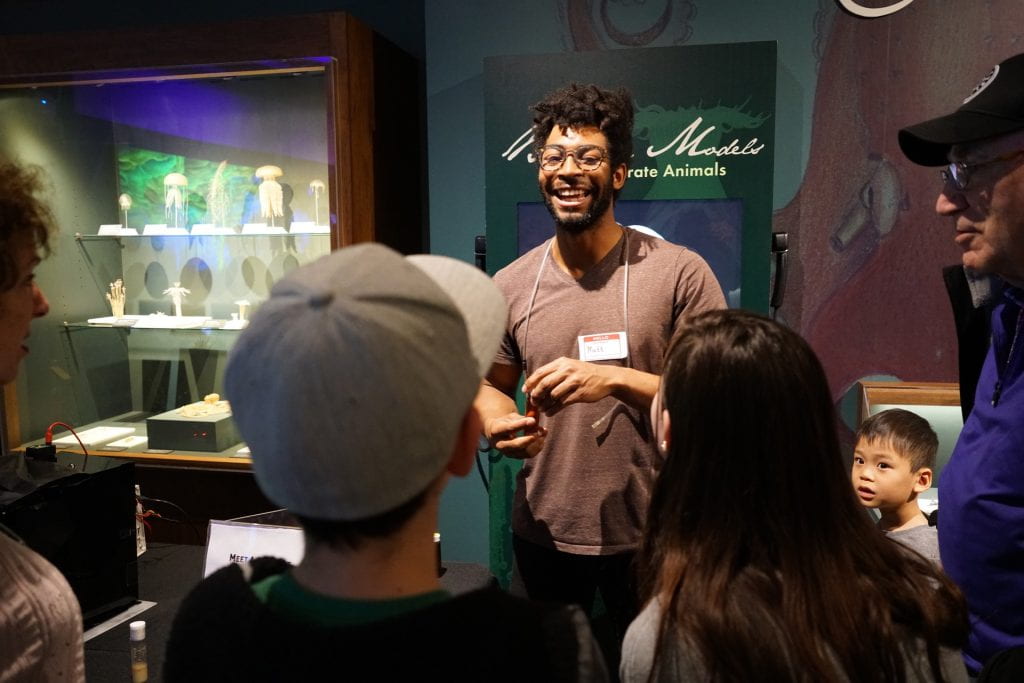 Black man speak to a group of adults and kids in the Sea Creatures gallery.