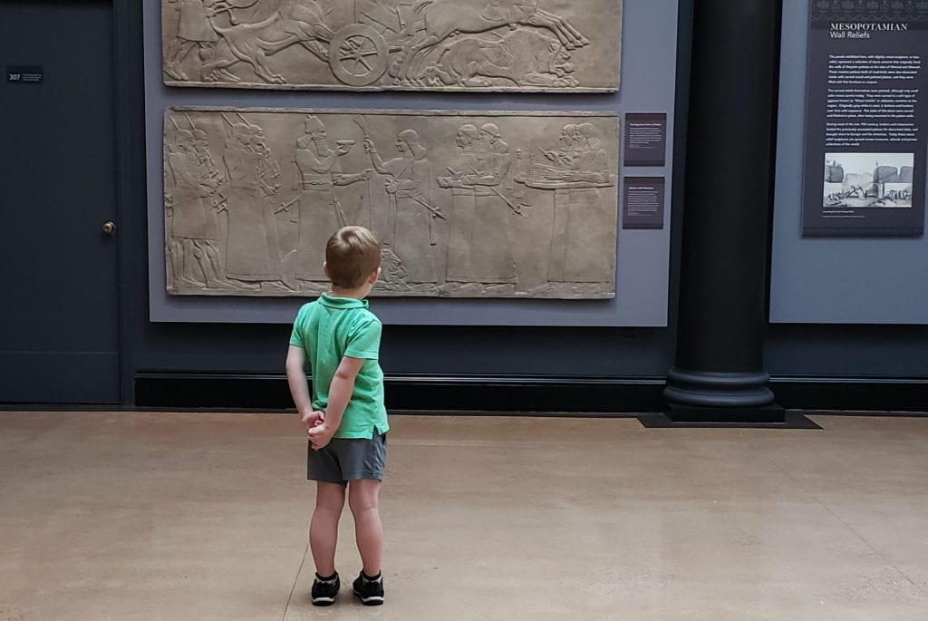 A boy standing in front of Mesopotamian reliefs.