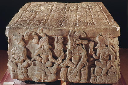 A square stone monument with Maya glyphs etched in.