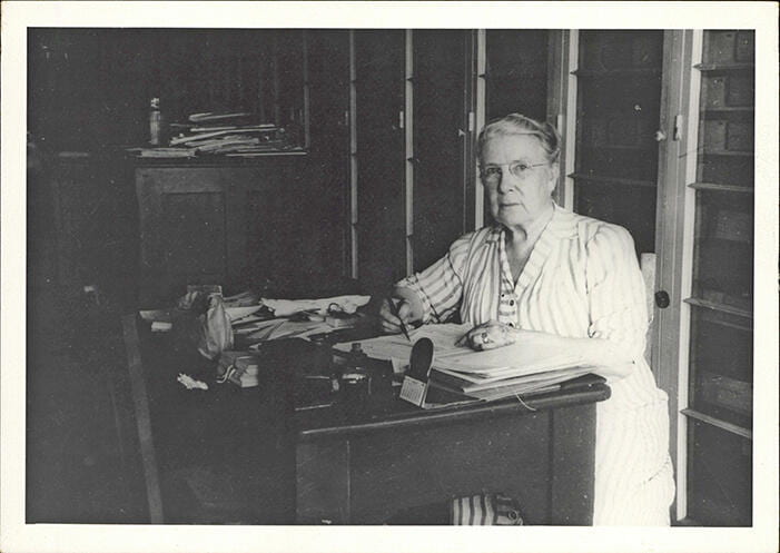 A black and white photo of a woman working at a desk.