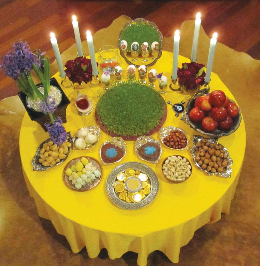 Round table with a bright yellow tablecloth with a bountiful of foods, flowers and candles laid out.