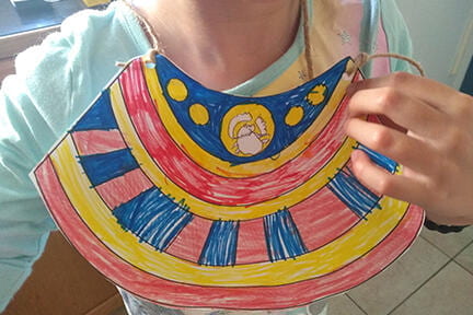 Girl holding a colorful, handmade scarab beetle necklace.