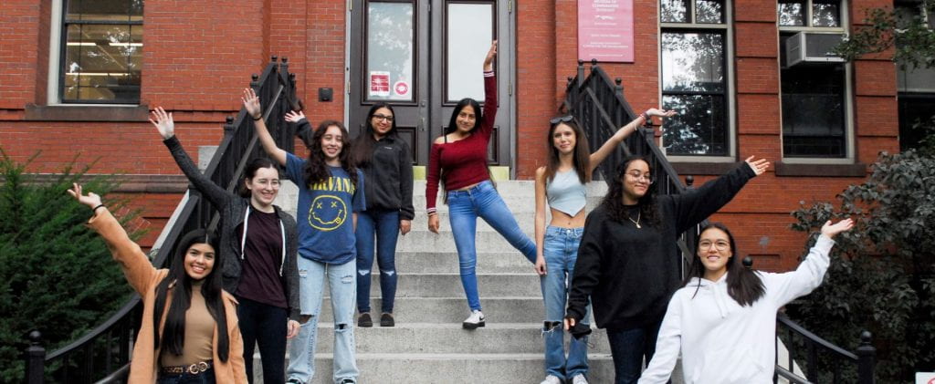 Eight latina high school girls lined cheering on stairs.