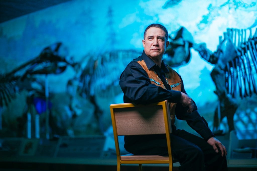 Lawrence Bradley sitting on a chair in front of a display of dinosaurs.
