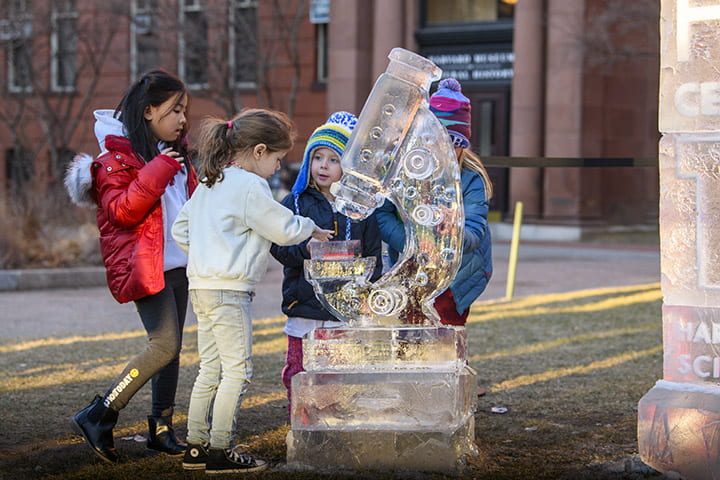 A group of children surrounding an ice sculpture of a microscope.