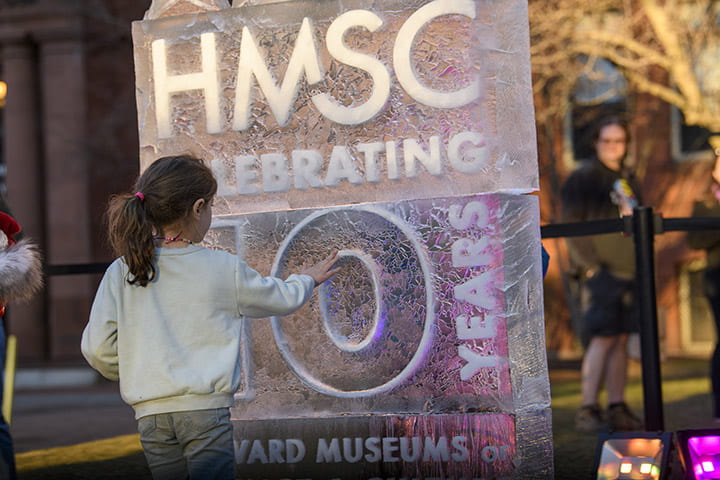 A child closely inspecting an ice sculpture of the HMSC 10 year logo.