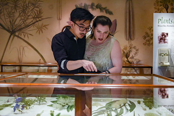 A woman and a man stand close to each other looking at a glass flower model.