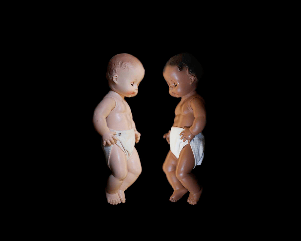 Two baby dolls in diapers presented on a black backdrop.